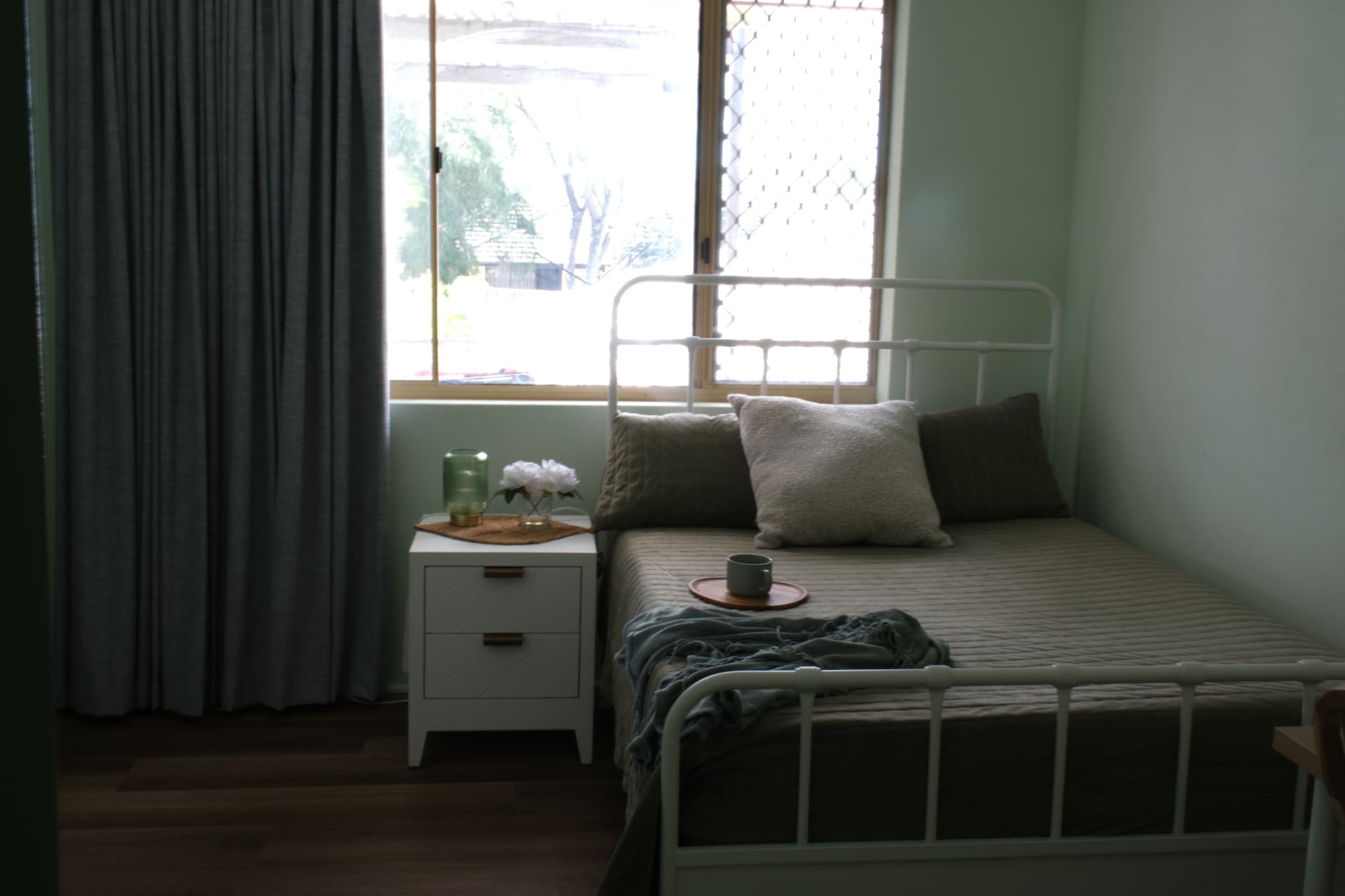 A lodge bedroom with soft green walls, white bed frame and timber flooring